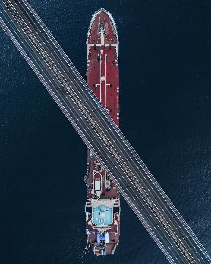 A stunning aerial view capturing a bridge crossing over a large ship in coastal waters.